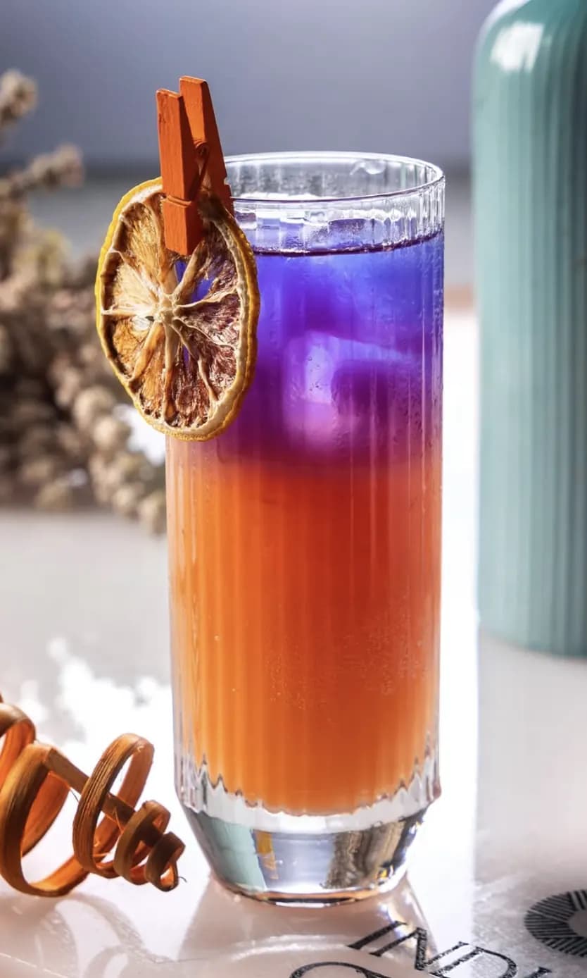 Layered orange and blue cocktail with dried orange garnish