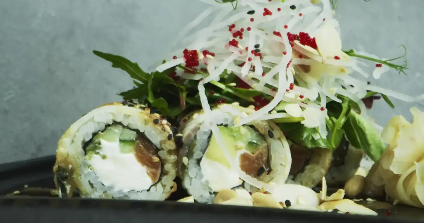 Chef finishing sushi rolls with sesame seeds