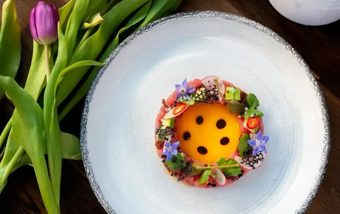 Tuna tartare with egg yolk and edible flowers on a white ceramic plate