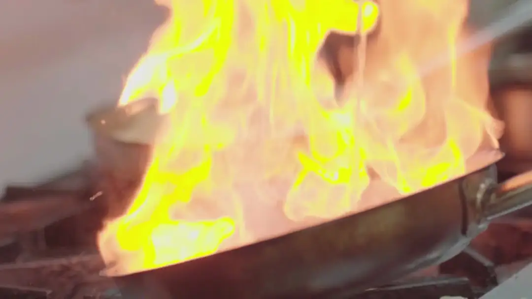 Chef working over open flames on a commercial kitchen range